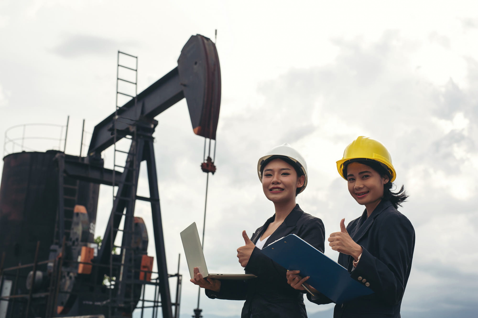 Two field engineers giving a thumbs up in front of an oil pumpjack